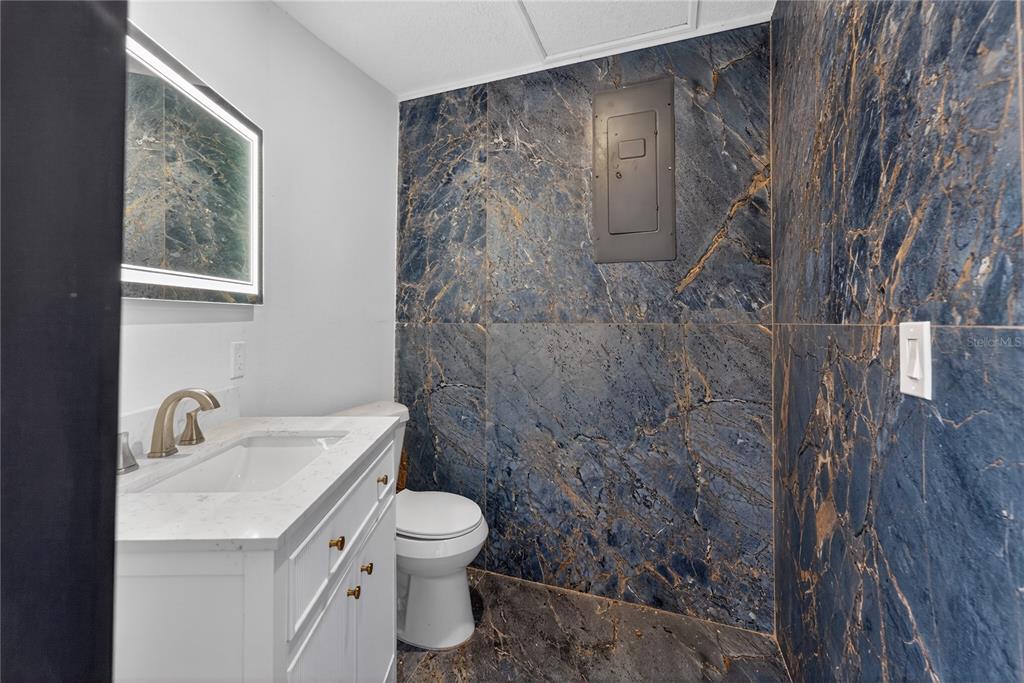 A bathroom features a white vanity, a toilet, and walls covered in blue marble tile — 305 SWEETWATER CLUB CIRCLE, LONGWOOD, FL