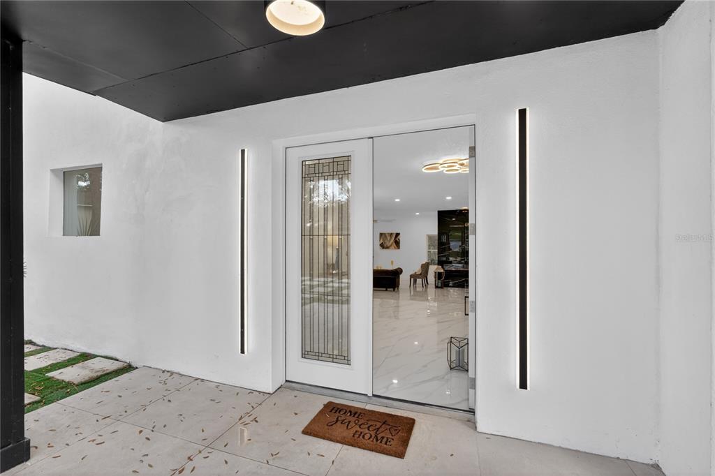 A modern front entryway features a glass-paneled door, vertical wall lights, and white flooring — 305 SWEETWATER CLUB CIRCLE, LONGWOOD, FL