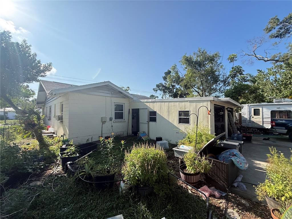 The exterior of a light-colored house features a side yard with potted plants and vegetation — 714 26TH STREET W, BRADENTON, FL