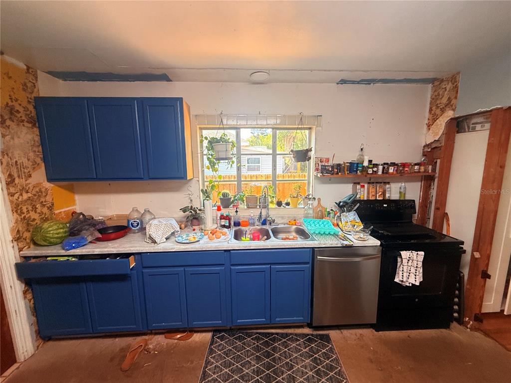 A kitchen features blue cabinets, a stainless steel dishwasher, and unfinished walls with exposed studs — 714 26TH STREET W, BRADENTON, FL