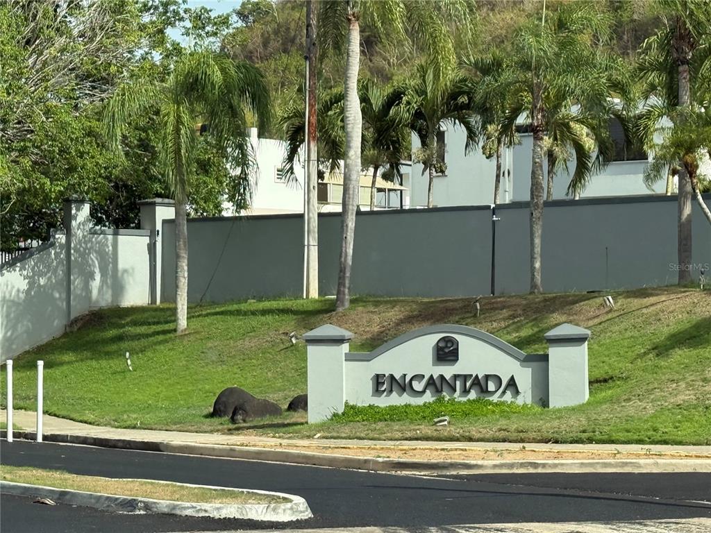 A stone monument sign reading Encantada sits on a grassy hill in front of a wall — 3 SE . UNIT PG 133, TRUJILLO ALTO, PR