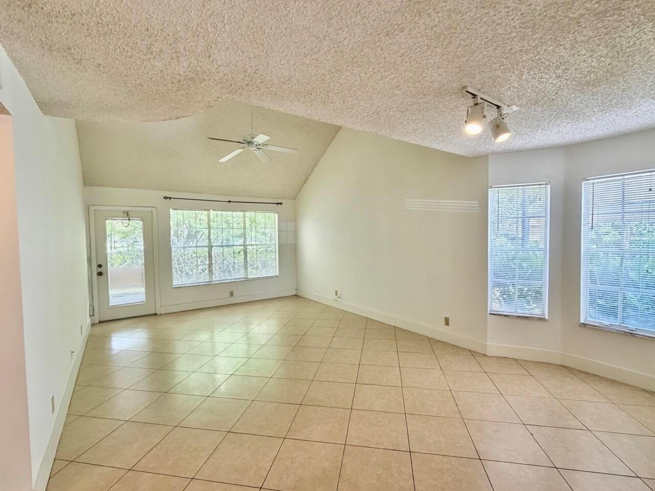 An empty living room features vaulted ceilings, a ceiling fan, tile flooring, and large windows — 6308 La Costa Drive # D, Boca Raton FL 33433, BOCA RATON, FL