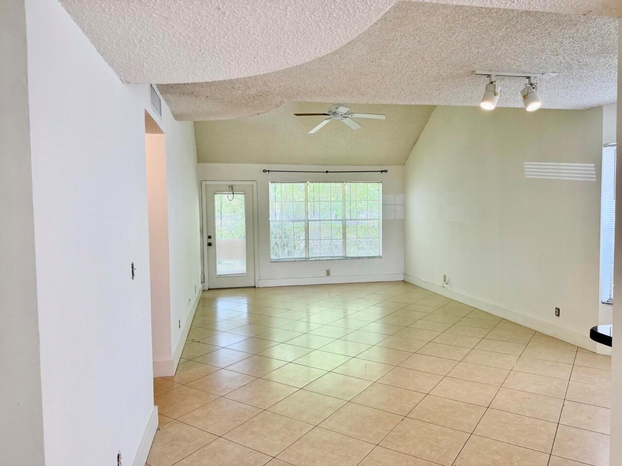 An empty living room features vaulted ceilings, beige tile flooring, and a glass-paneled exterior door — 6308 La Costa Drive # D, Boca Raton FL 33433, BOCA RATON, FL