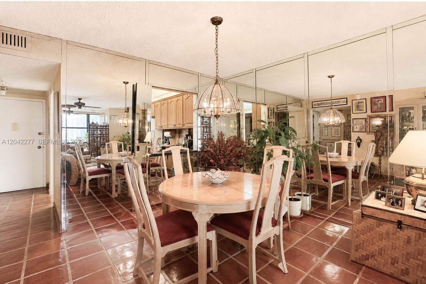 A dining room features a round wooden table, chairs, tile flooring, and mirrored wall panels — 1000 Parkview Dr # 726, Hallandale Beach FL 33009, HALLANDALE BEACH, FL