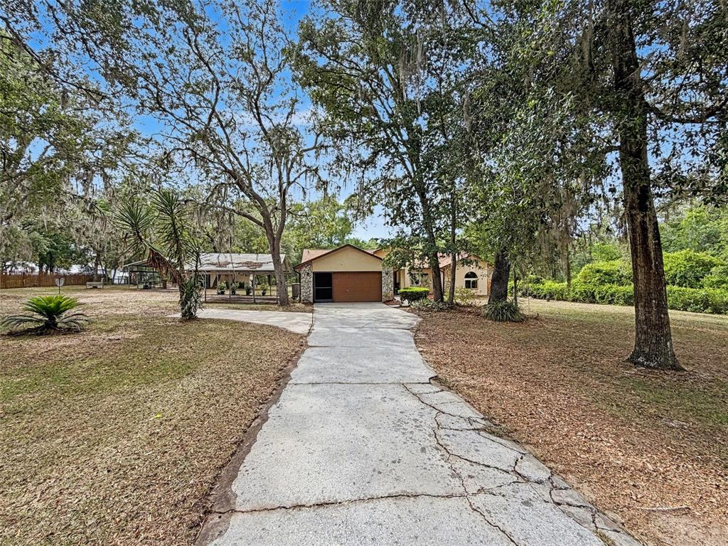 A house and a detached garage stand on a large, grassy lot with mature trees — 7111 RICKER AVENUE, WEBSTER, FL