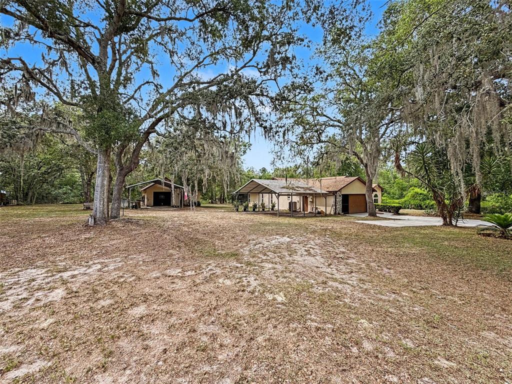 A house and a detached garage with carports sit on a large, tree-covered lot — 7111 RICKER AVENUE, WEBSTER, FL