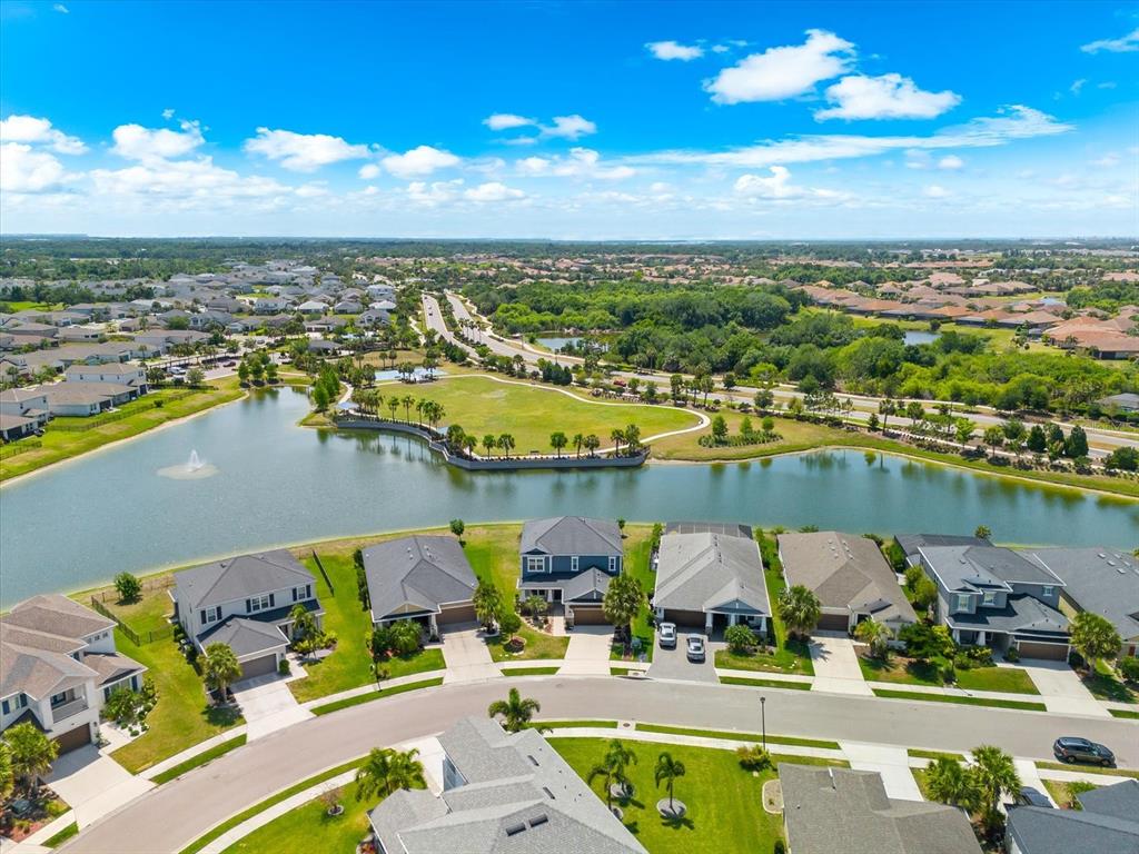 An aerial view shows suburban houses bordering a lake with a central grassy park area — 5633 MAIDENSTONE WAY, PALMETTO, FL