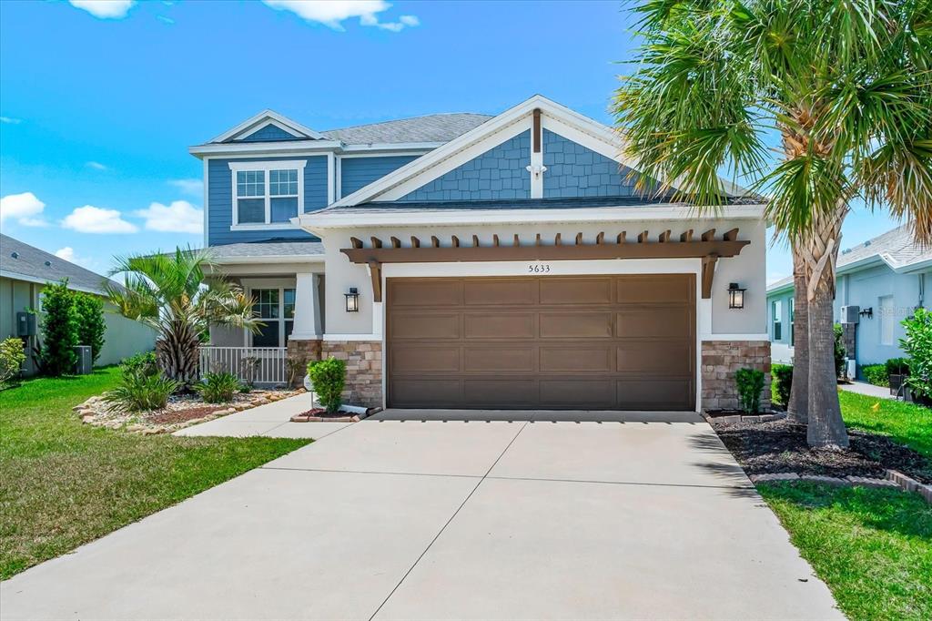 A two-story house with a brown garage door, stone accents, and a wooden pergola — 5633 MAIDENSTONE WAY, PALMETTO, FL
