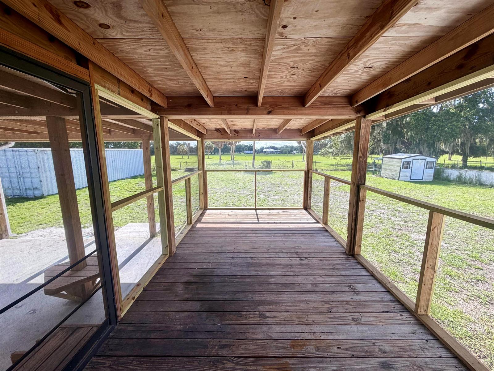 A covered wooden deck with railings overlooks a grassy yard with two small outbuildings — 2822 SE 47th Terrace, Okeechobee FL 34974, OKEECHOBEE, FL