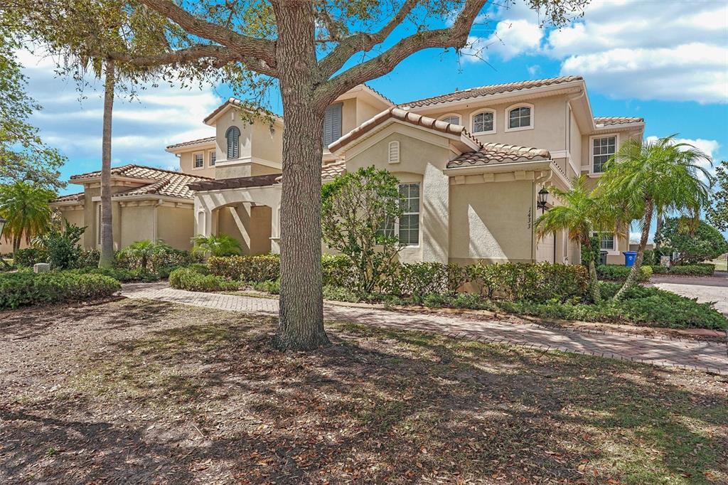 A two-story stucco house with a tile roof and a brick walkway under a tree — 1435 EMERALD DUNES DRIVE, SUN CITY CENTER, FL