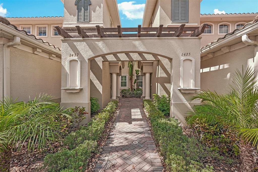 A brick walkway leads to a covered entryway between two beige stucco building units — 1435 EMERALD DUNES DRIVE, SUN CITY CENTER, FL