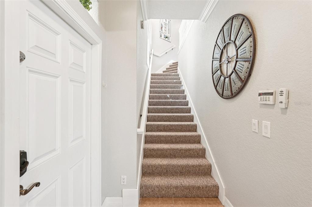 A carpeted staircase leads upward next to a white door and a large wall clock — 1435 EMERALD DUNES DRIVE, SUN CITY CENTER, FL