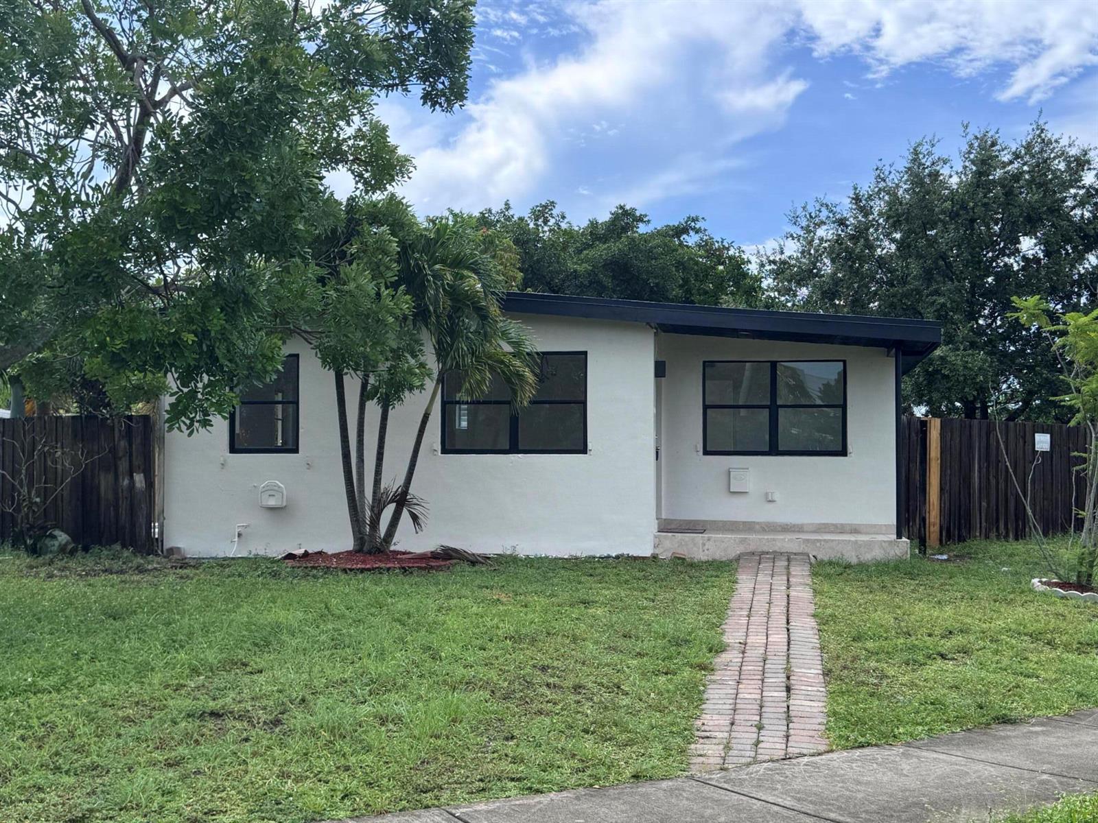 A white, single-story house with a brick walkway and black-framed windows sits on a lawn — 4310 NE 13th Avenue, Pompano Beach FL 33064, POMPANO BEACH, FL