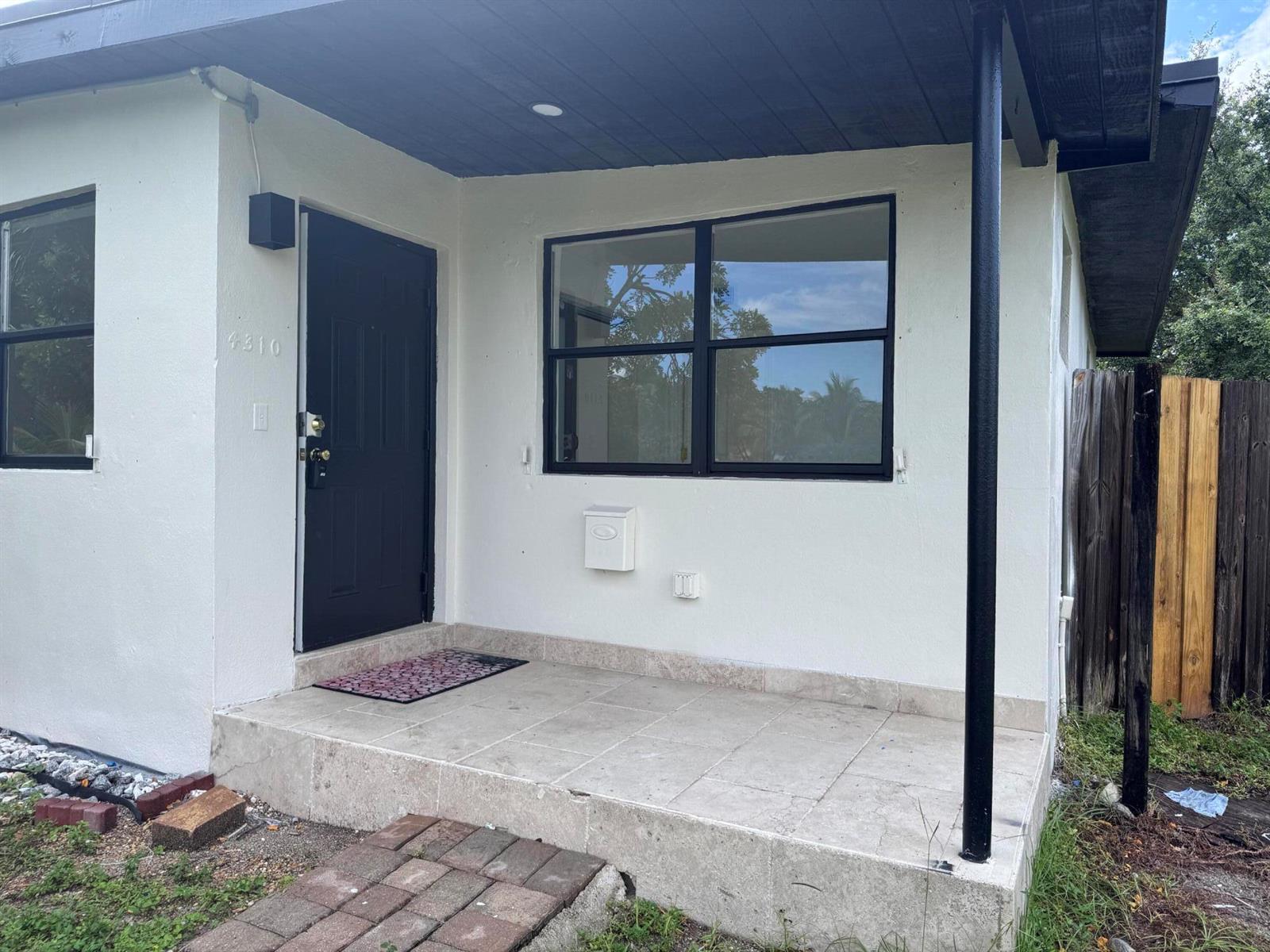 A white house exterior features a black front door, a large window, and a tiled porch — 4310 NE 13th Avenue, Pompano Beach FL 33064, POMPANO BEACH, FL