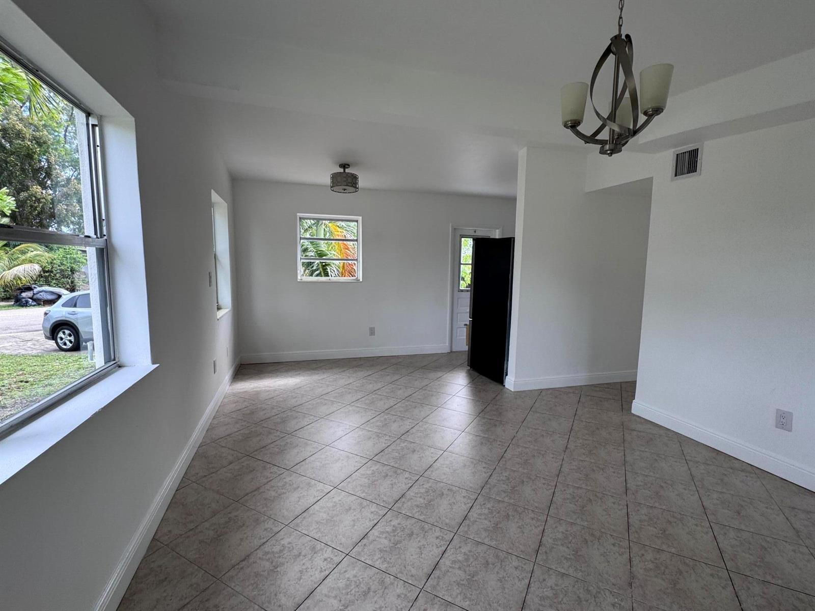 An empty room features white walls, tile flooring, a chandelier, and a large window — 4310 NE 13th Avenue, Pompano Beach FL 33064, POMPANO BEACH, FL