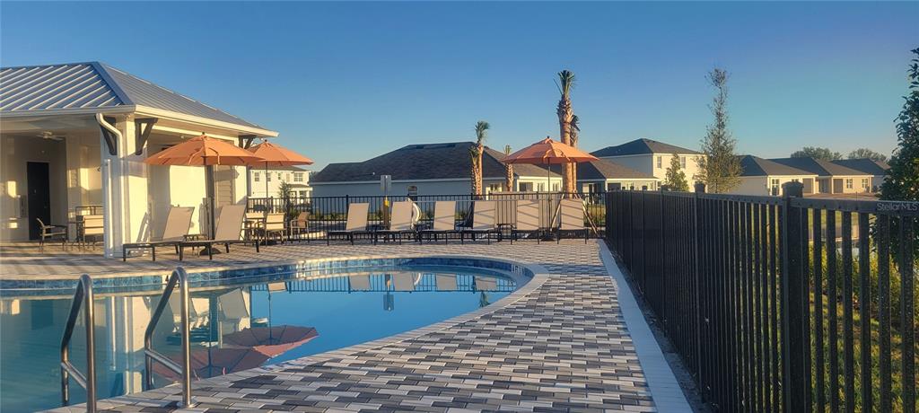 A swimming pool with lounge chairs and umbrellas sits beside a community building and fence — 10908 38TH TERRACE EAST, PALMETTO, FL