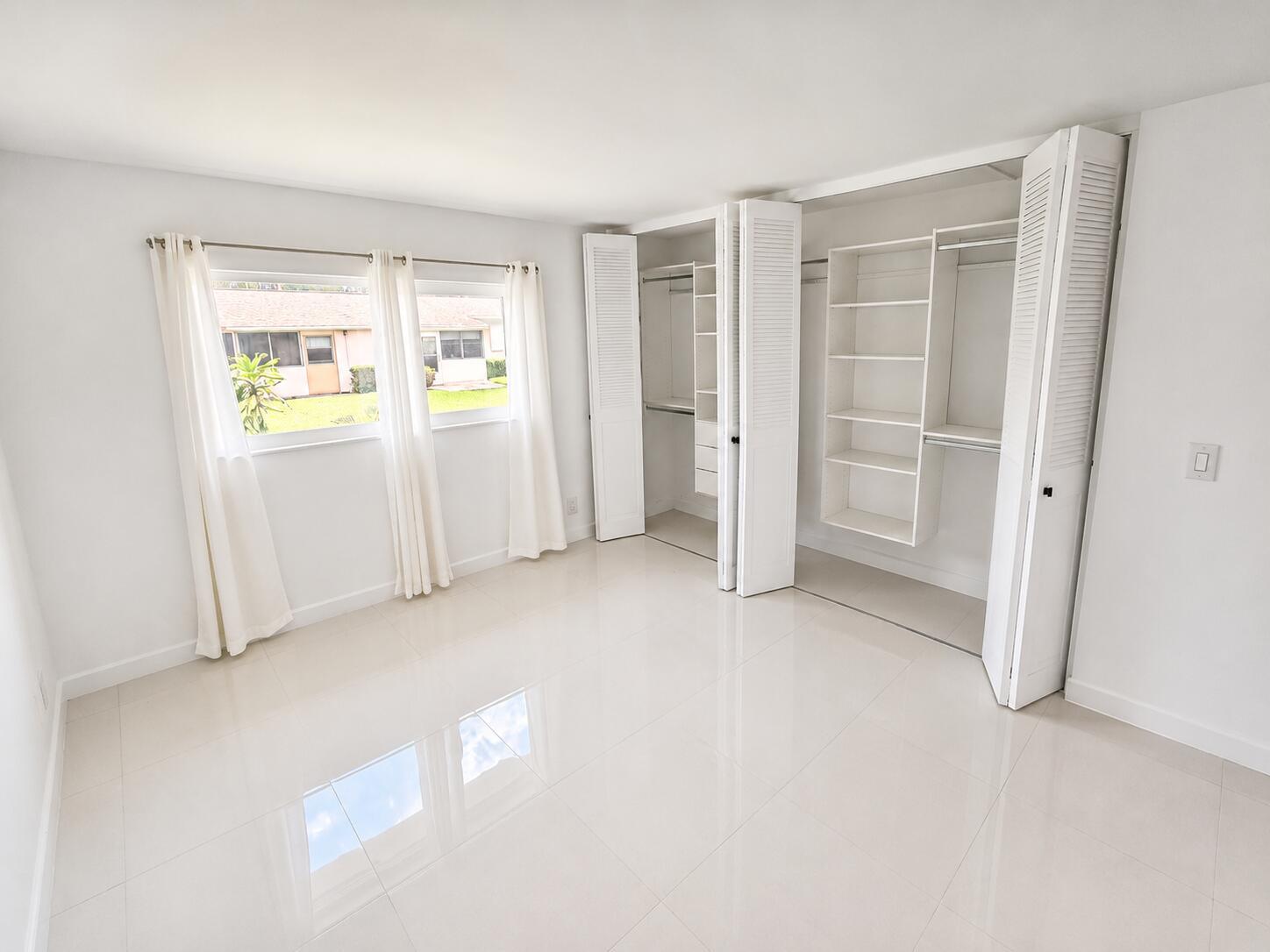 A bright bedroom with white walls, glossy tile floors, and a large built-in closet — 2568 Dudley Drive E # G, West Palm Beach FL 33415, WEST PALM BEACH, FL