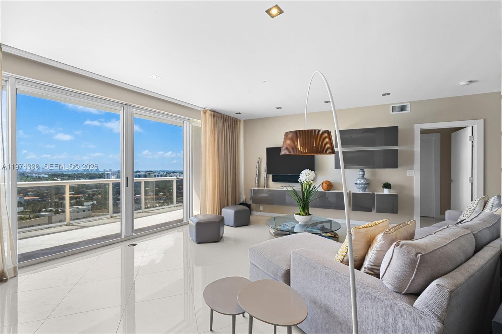 A modern living room features white tile floors, a grey sectional, and a balcony view — 9601 Collins Ave # 1208, Bal Harbour FL 33154, BAL HARBOUR, FL