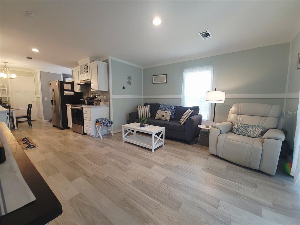 A living room with light wood-look flooring, a dark sofa, and a white recliner — 3531 SE 173RD TERRACE, OCKLAWAHA, FL