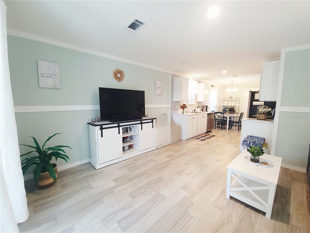 A living room with light green walls, wood-look tile floors, and an open kitchen area — 3531 SE 173RD TERRACE, OCKLAWAHA, FL