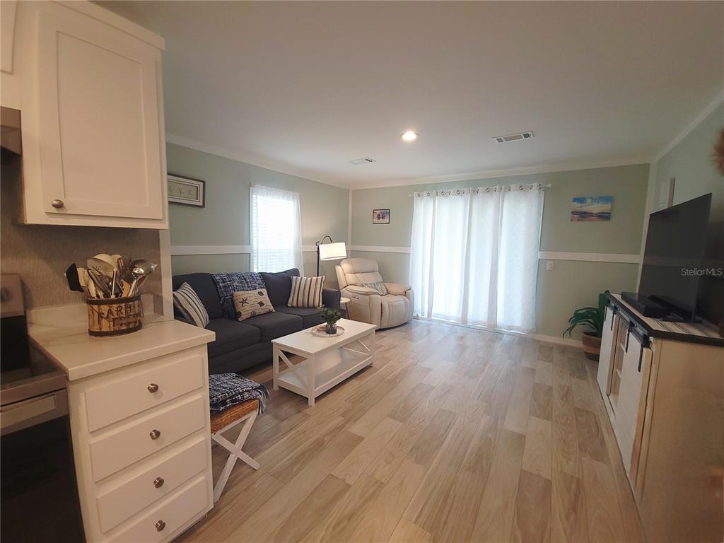 A living room features light wood-look flooring, a blue sofa, and a white media console — 3531 SE 173RD TERRACE, OCKLAWAHA, FL