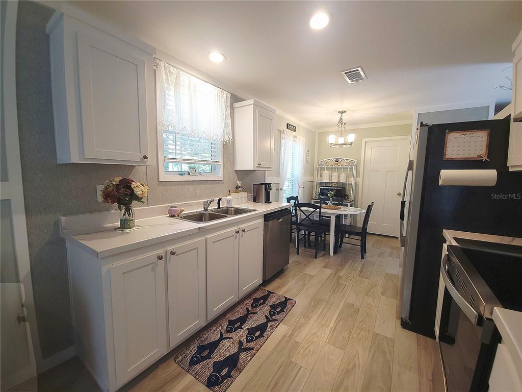 A kitchen features white cabinets, stainless steel appliances, a dining area, and wood-look flooring — 3531 SE 173RD TERRACE, OCKLAWAHA, FL