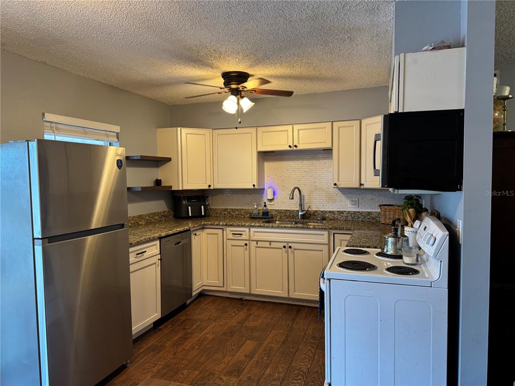 A kitchen features white cabinets, stainless steel appliances, granite countertops, and wood-look flooring — 580 FERN AVENUE, TAVARES, FL
