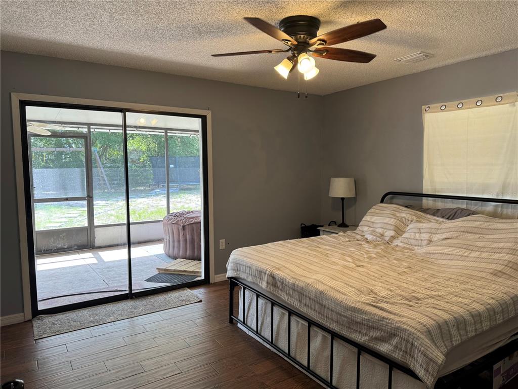 A bedroom with wood-look tile floors, a ceiling fan, and sliding doors to a patio — 580 FERN AVENUE, TAVARES, FL