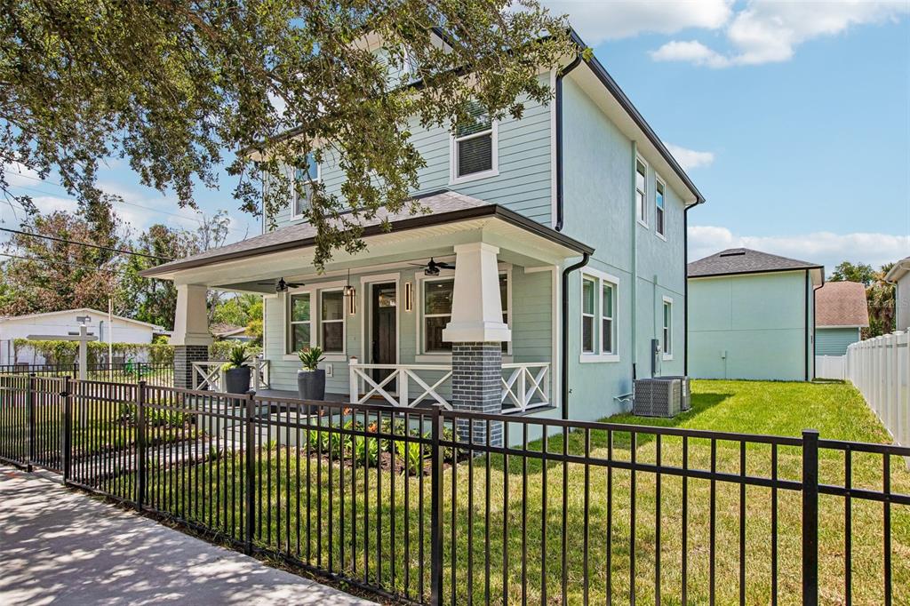 A light blue two-story house with a covered front porch and a black metal fence — 406 E CHELSEA STREET, TAMPA, FL