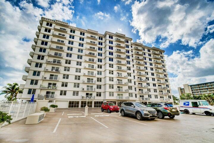 A multi-story white apartment building with balconies stands above a parking lot with several vehicles — 3221 S Ocean Boulevard # 207, Highland Beach FL 33487, HIGHLAND BEACH, FL