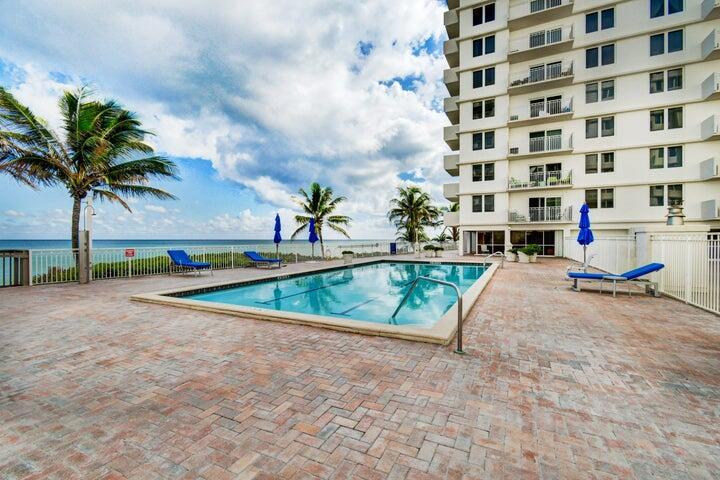 A rectangular swimming pool sits on a brick patio beside a multi-story apartment building — 3221 S Ocean Boulevard # 207, Highland Beach FL 33487, HIGHLAND BEACH, FL