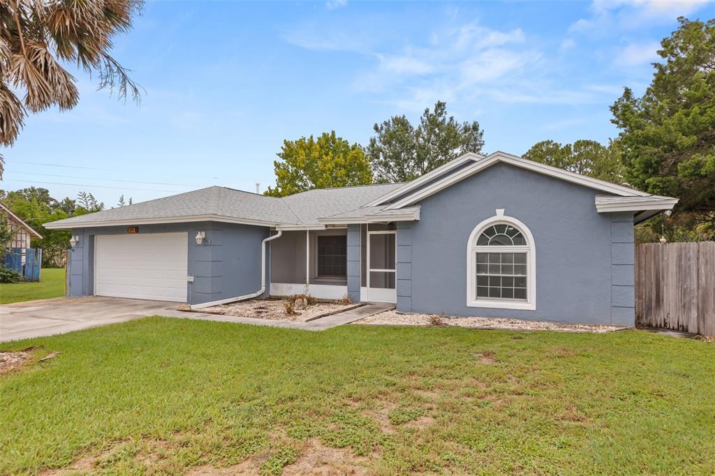 A single-story blue house with a white garage door, arched window, and a front lawn — 2556 TANDORI CIRCLE, ORLANDO, FL