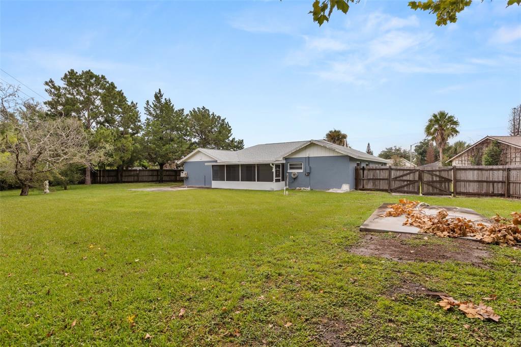 The backyard of a single-story house features a screened-in porch and a wooden fence — 2556 TANDORI CIRCLE, ORLANDO, FL