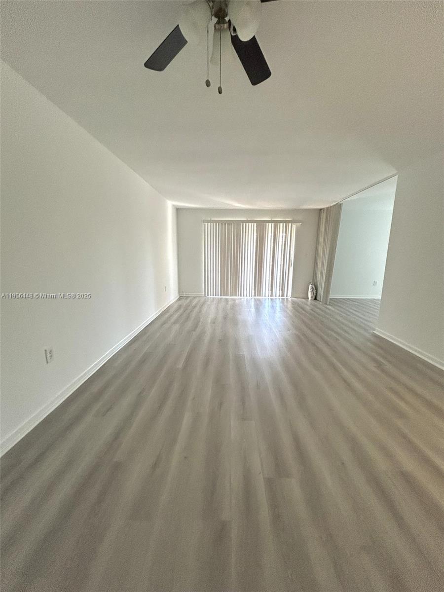 An empty living room features light-colored wood-look flooring, white walls, and vertical window blinds — 11905 NE 2nd Ave # C402, North Miami FL 33161, NORTH MIAMI, FL
