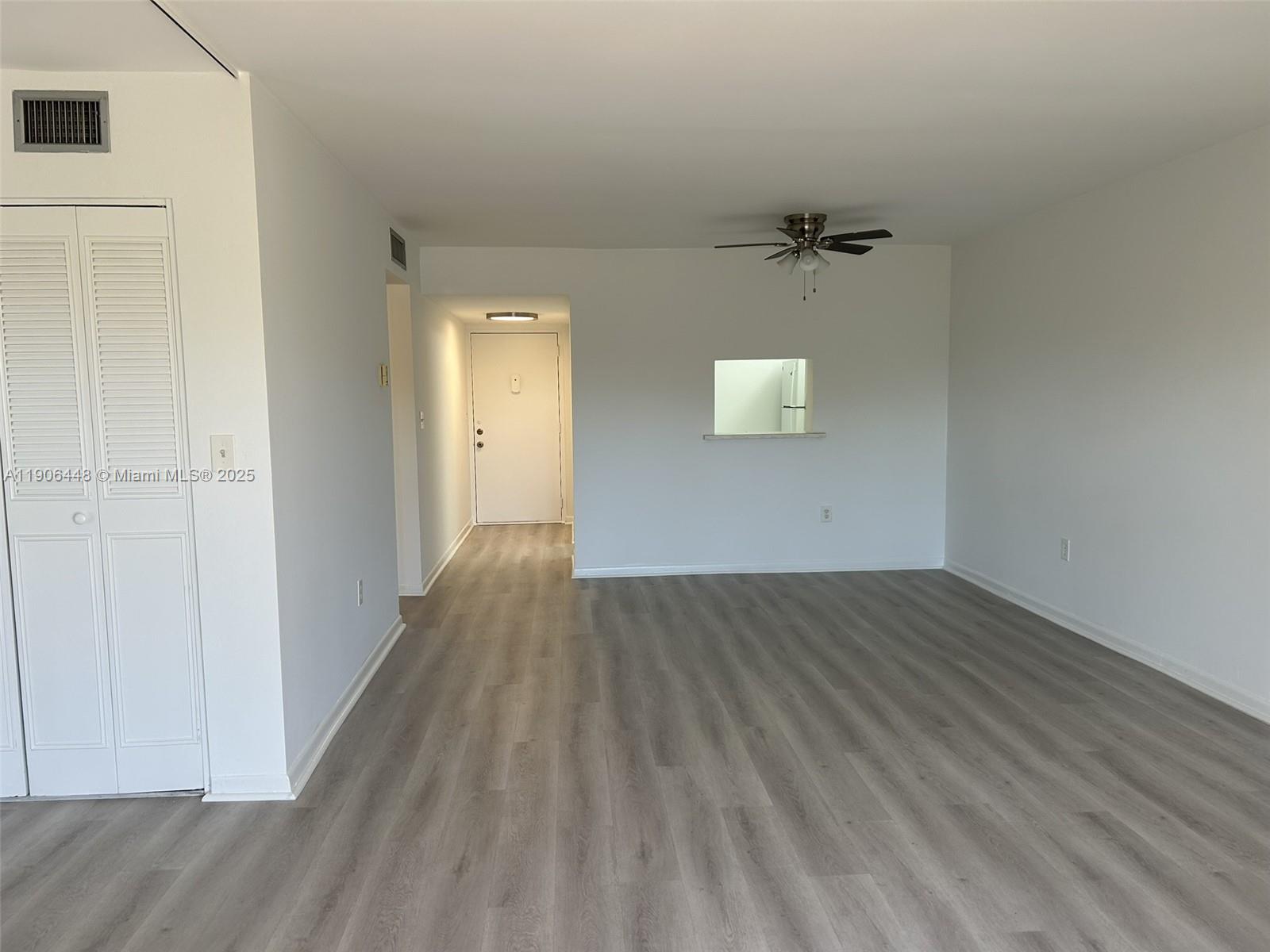 An empty room features white walls, gray wood-look flooring, a ceiling fan, and a pass-through window — 11905 NE 2nd Ave # C402, North Miami FL 33161, NORTH MIAMI, FL