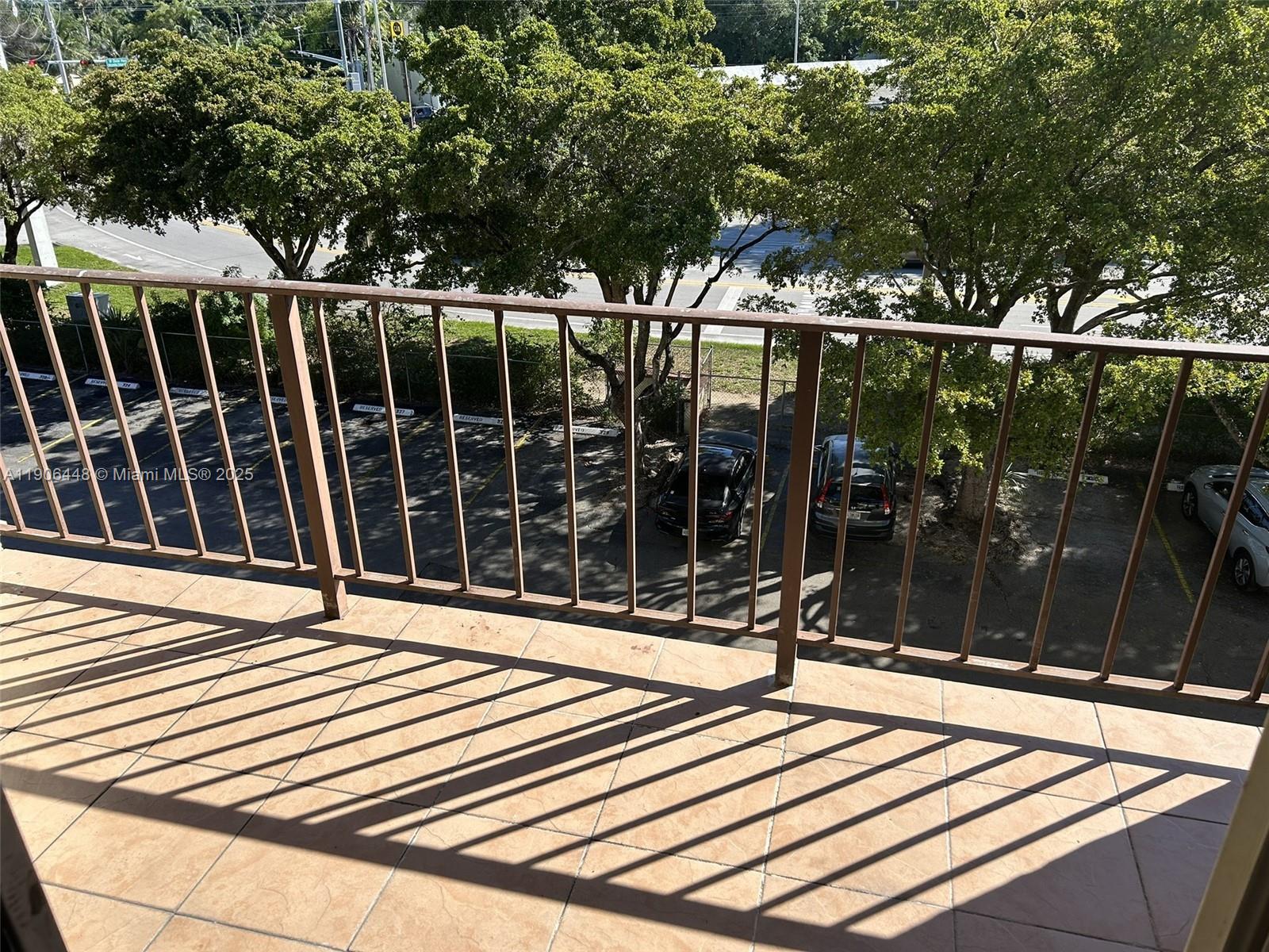 A balcony with tiled flooring and a metal railing overlooks a parking lot and trees — 11905 NE 2nd Ave # C402, North Miami FL 33161, NORTH MIAMI, FL