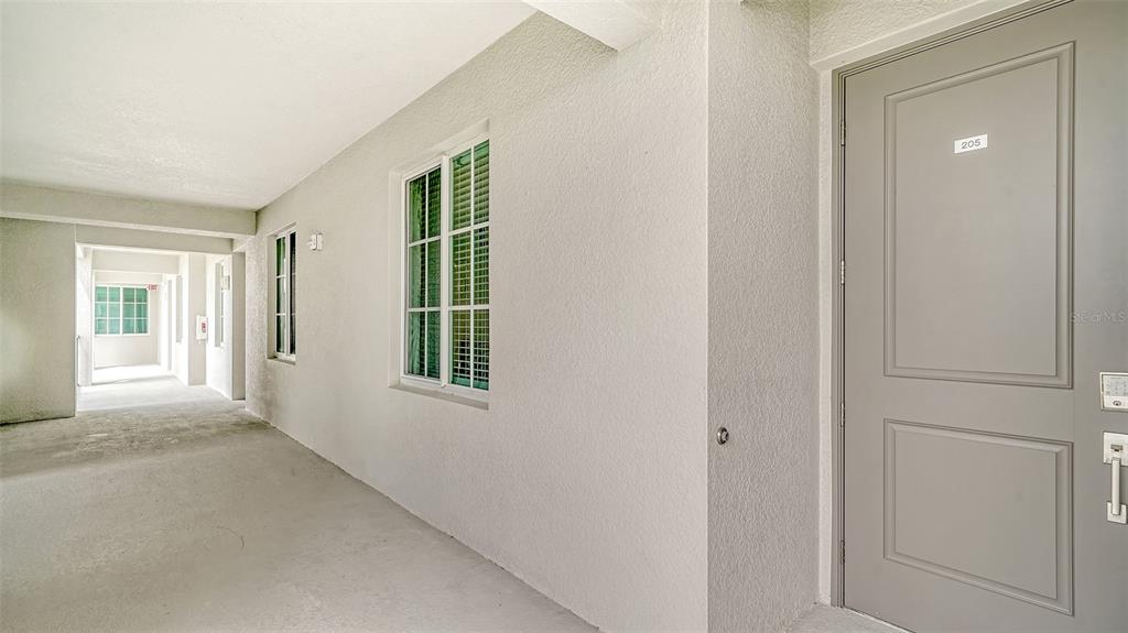 A gray door labeled 205 is located in a white-walled outdoor hallway with windows — 12180 WELLEN GOLF STREET UNIT 205, VENICE, FL