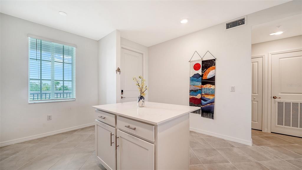 A kitchen island with white cabinets and a quartz countertop sits in a tiled room — 12180 WELLEN GOLF STREET UNIT 205, VENICE, FL