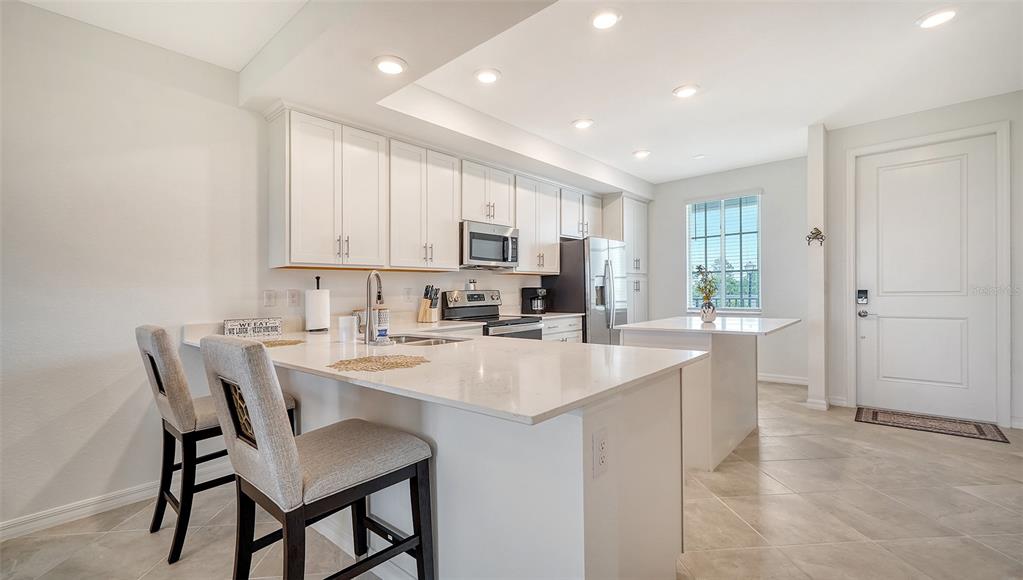 A modern kitchen features white cabinetry, quartz countertops, a breakfast bar, and stainless steel appliances — 12180 WELLEN GOLF STREET UNIT 205, VENICE, FL