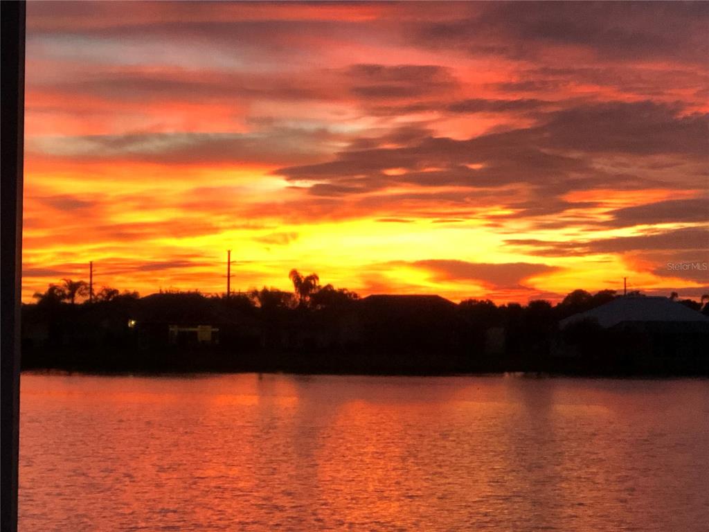 A vibrant sunset glows over a calm lake with silhouettes of houses and trees — 12942 SW KINGSWAY CIRCLE, LAKE SUZY, FL