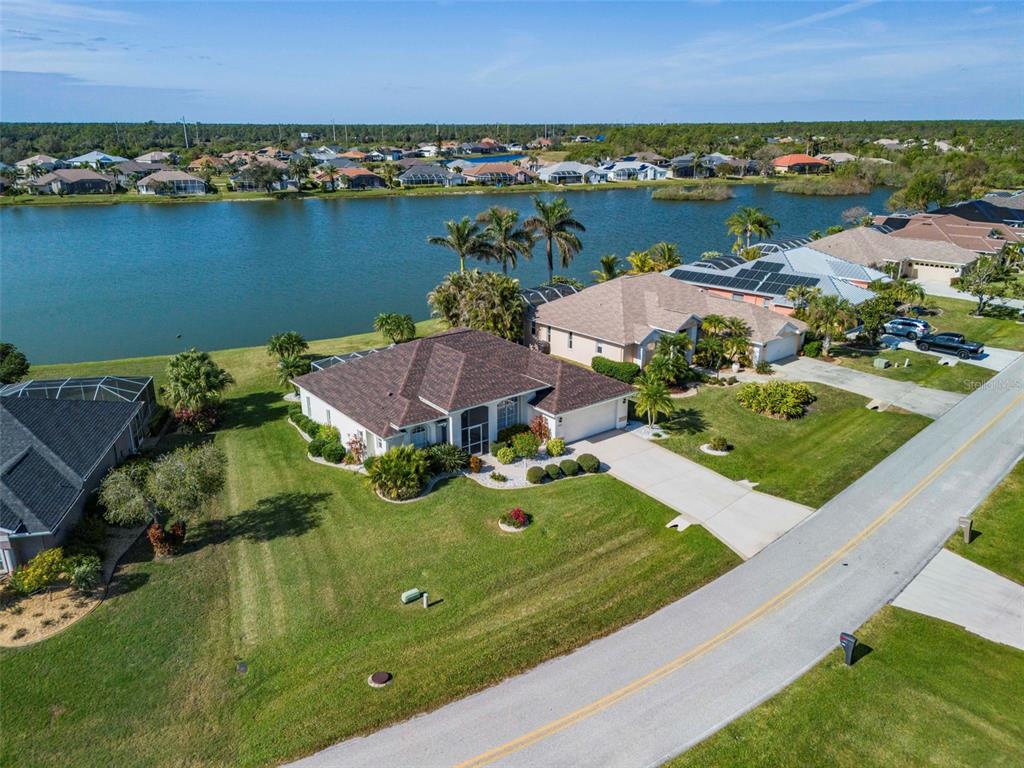 An aerial view shows a single-story house with a brown roof beside a lake — 12942 SW KINGSWAY CIRCLE, LAKE SUZY, FL
