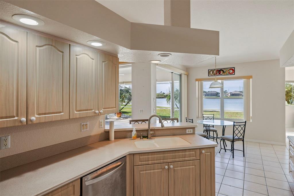 A kitchen with light wood cabinets and a sink overlooks a dining area and lake — 12942 SW KINGSWAY CIRCLE, LAKE SUZY, FL