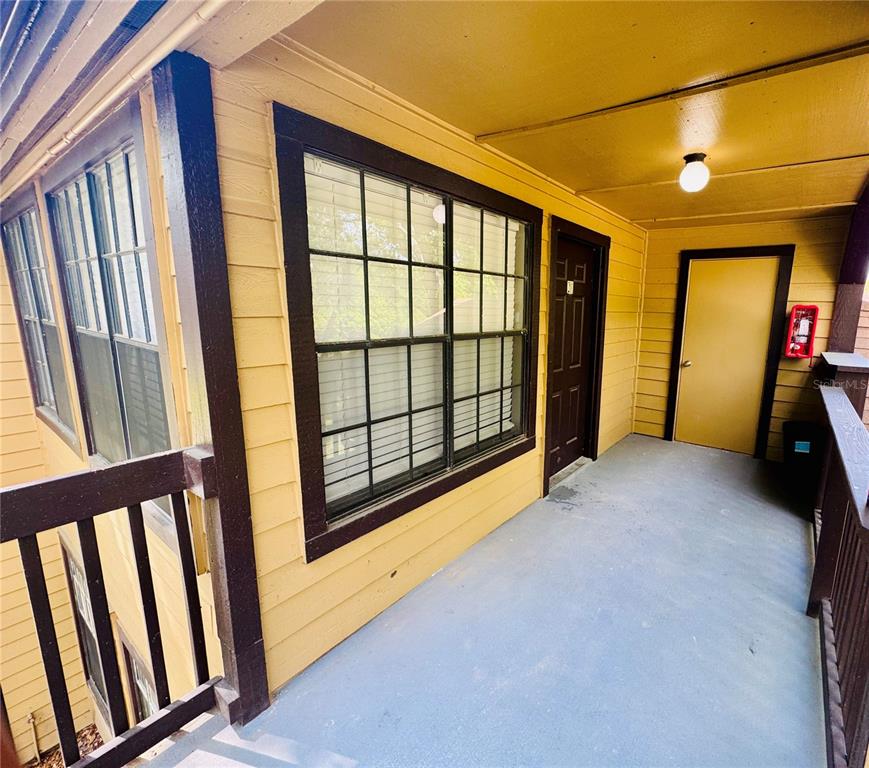 An exterior view of a covered apartment balcony with yellow siding and a dark door — 385 WOODSIDE DRIVE UNIT 201, ALTAMONTE SPRINGS, FL