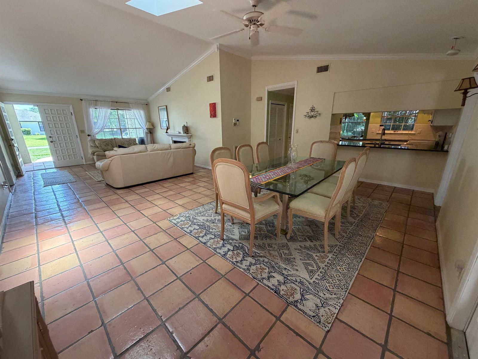An open-concept living and dining area features terracotta tile floors, a vaulted ceiling, and skylights — 1290 5th Place, Vero Beach FL 32962, VERO BEACH, FL