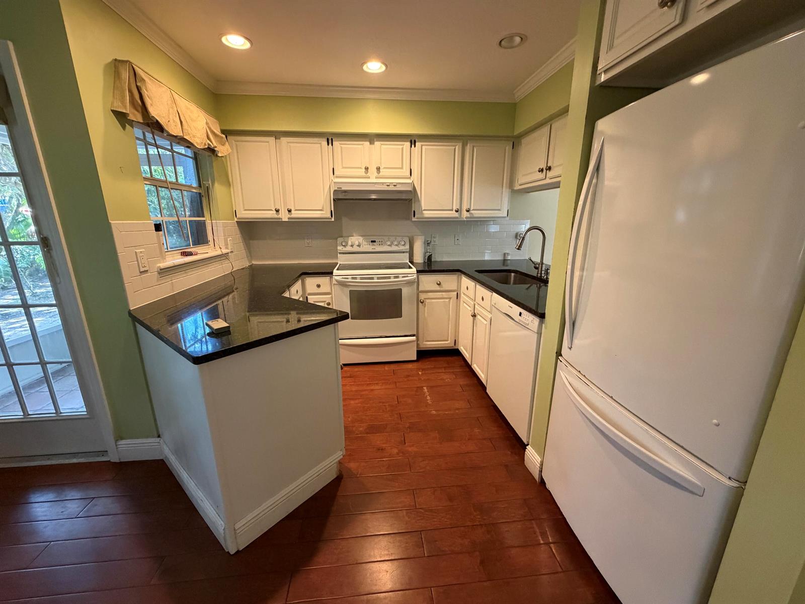 A kitchen features white cabinets, black countertops, stainless steel appliances, and wood flooring — 1290 5th Place, Vero Beach FL 32962, VERO BEACH, FL