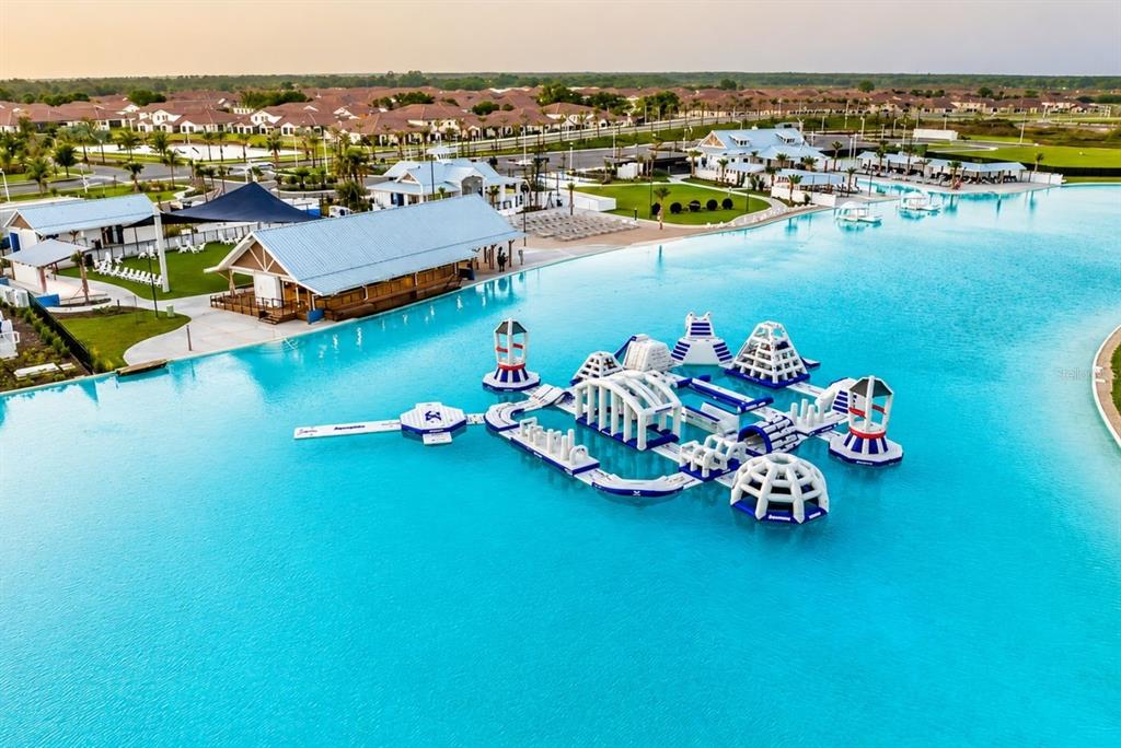 An aerial view shows a large blue lagoon with an inflatable obstacle course and buildings — 7562 SEA OAK COURT, PARRISH, FL