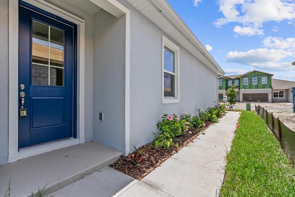 A blue front door opens to a concrete walkway beside a house with flower beds — 7562 SEA OAK COURT, PARRISH, FL