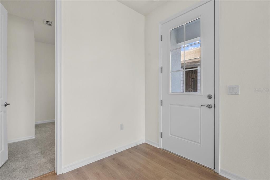 An entryway features light wood-look flooring, white walls, and a white door with glass panels — 7562 SEA OAK COURT, PARRISH, FL