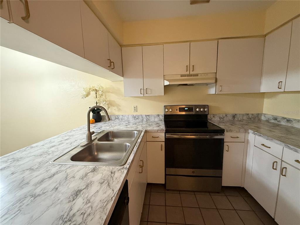 A kitchen features white cabinets, marble-patterned laminate countertops, and stainless steel appliances — 2735 SW 35TH PLACE UNIT 1604, GAINESVILLE, FL