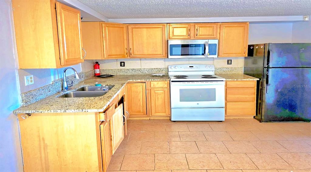 A kitchen features light wood cabinets, granite countertops, white appliances, and beige tile flooring — 3806 BADEN DRIVE, HOLIDAY, FL